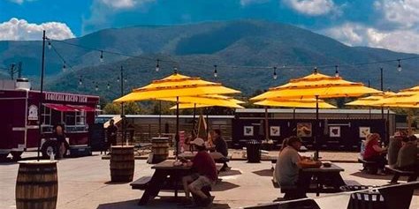 An open-air food park in Wears Valley — picnic tables under yellow umbrellas, food trucks, and the ridge behind.